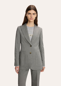 A model wearing a tailored pinstripe blazer over a white collared shirt and dark vest, paired with a matching pleated mini skirt, photographed against a plain light background.