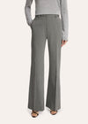 A model stands against a light studio background wearing a tailored light gray pinstripe suit with a white shirt, patterned tie, and black pointed shoes.